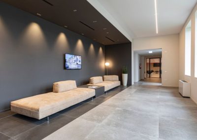 Elegante sala d'attesa aziendale con divani beige, parete grigia retroilluminata e pavimentazione in gres nella sede di Zini Elio S.r.l.