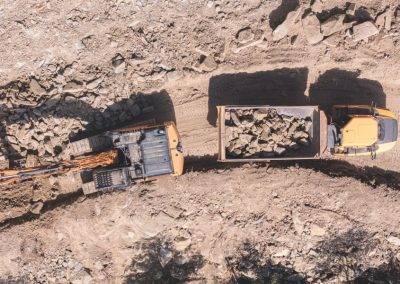 Veduta aerea zenitale di un escavatore cingolato e un dumper da cantiere carico di massi durante un lavoro di Zini Elio S.r.l.