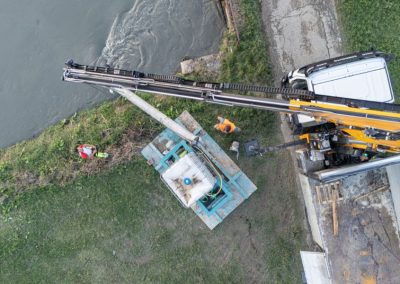 Veduta aerea zenitale di un camion gru Zini Elio S.r.l. che posiziona un'idrovora sull'argine di un fiume