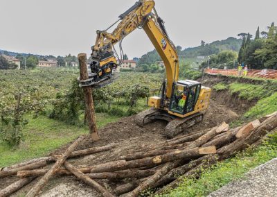 Escavatore idraulico Caterpillar attrezzato con pinza speciale per la posa di pali in legno durante un consolidamento versanti di Zini Elio S.r.l.